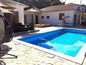 Une piscine avec une terrasse carrelée, une chaise longue et une petite table.