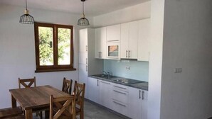 A modern kitchen with white cabinets, a wooden dining table, and pendant lighting. - Holiday home Sintija (Rab)