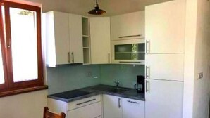 A compact kitchen with white cabinets, a wooden dining table, and chairs. - Holiday home Sintija (Rab)