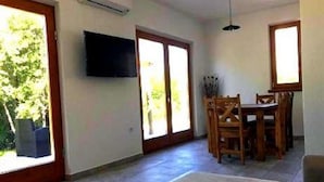 A spacious living area with a dining table and chairs, a flat-screen TV mounted on the wall, and large sliding glass doors leading to a garden. - Holiday home Sintija (Rab)