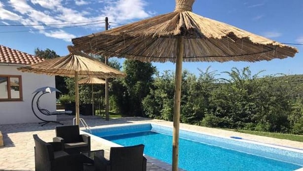 A swimming pool with a stone patio, outdoor furniture, and thatched umbrellas. - Holiday home Sintija (Rab)