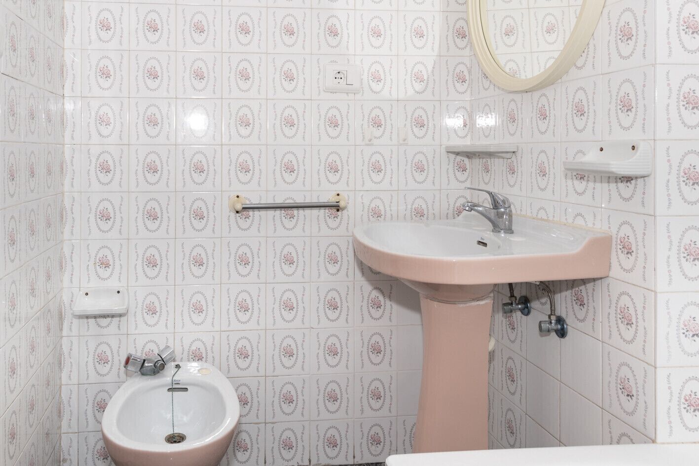 A bathroom with a pink sink, a mirror, and a small basin.