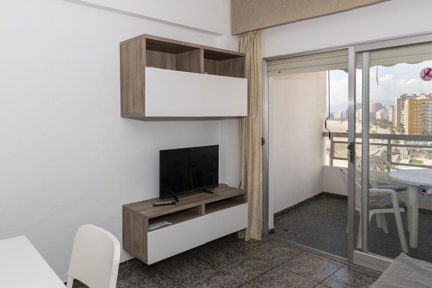 Un balcon avec une télévision, une petite table et des chaises.