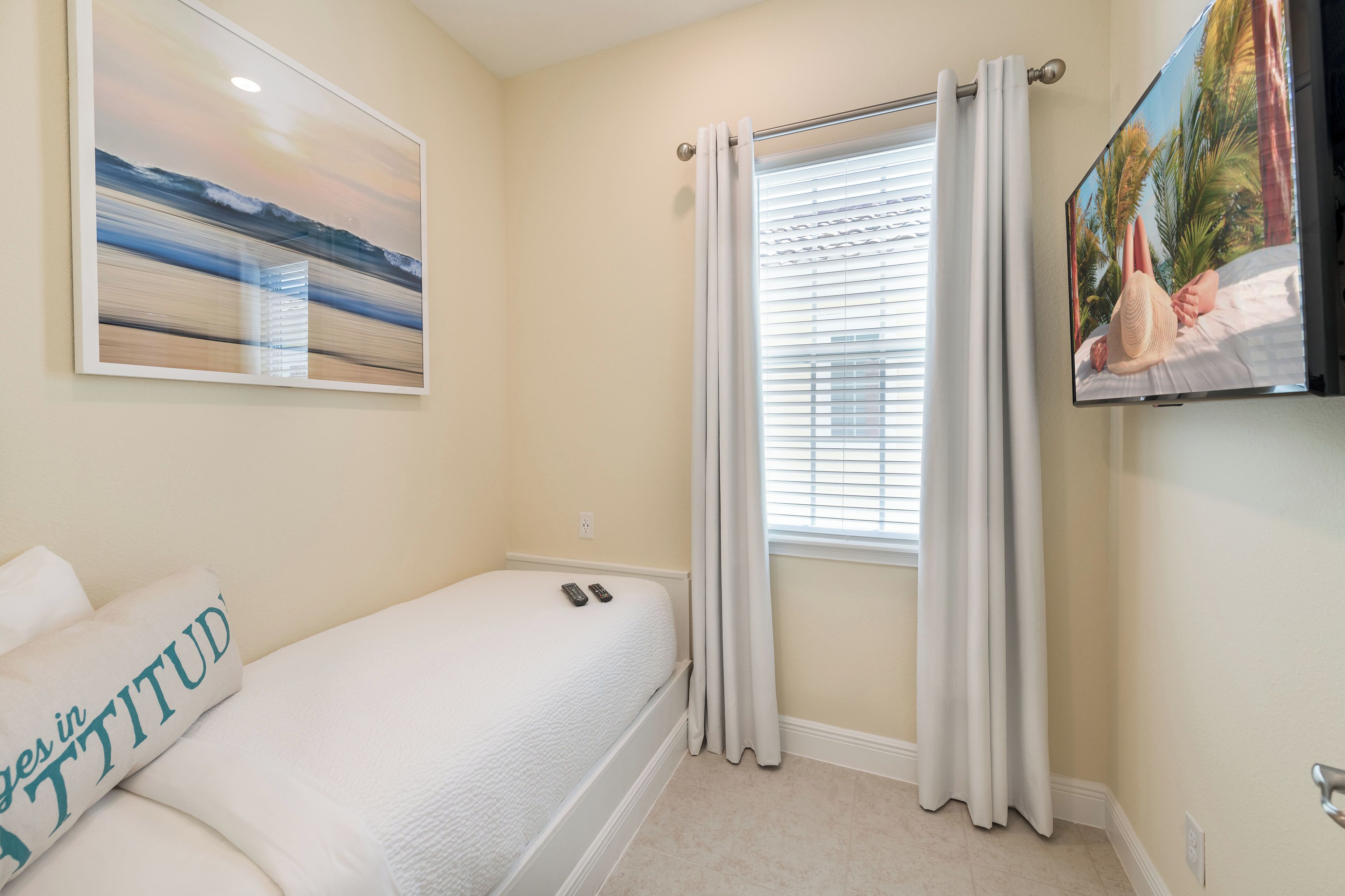 Un dormitorio con una cama, un cuadro de una playa, una ventana con persianas y un televisor en la pared.
