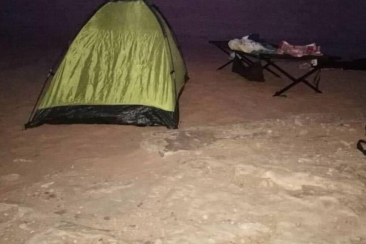 A tent set up on a sandy surface with a table nearby.