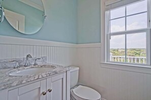 Ein Badezimmer mit Marmorwaschbecken, Toilette und einem Fenster mit Blick auf Grünfläche.