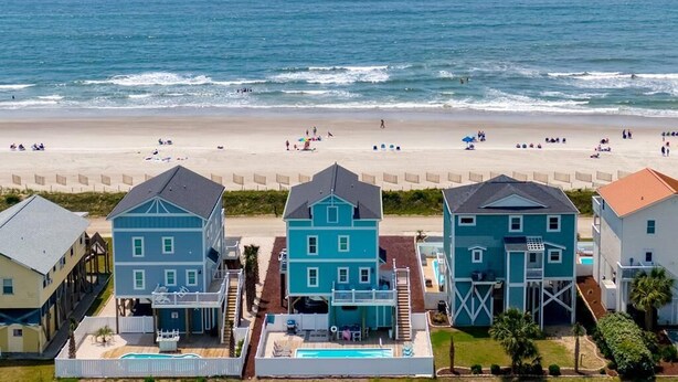Una propiedad frente a la playa con varias casas, una piscina y una playa al fondo.