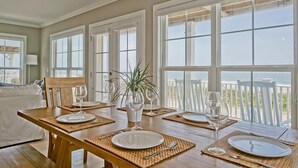 Un comedor con una mesa de madera preparada para cuatro personas, ventanas amplias y vista al océano.