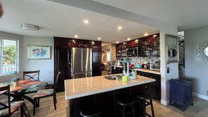 A modern kitchen with a central island, dark wood cabinets, stainless steel appliances, and a dining area with a table and chairs. - Home away from Home.Family & Pet friendly30+days (Canyon Lake)