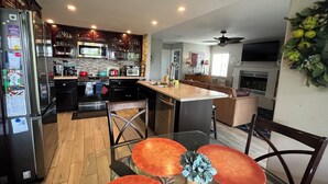 A modern kitchen with a central island, wooden flooring, and a dining area with round tables. - Home away from Home.Family & Pet friendly30+days (Canyon Lake)