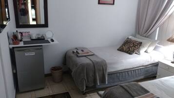 A bedroom with a bed, a small desk with a mirror, and a refrigerator.
