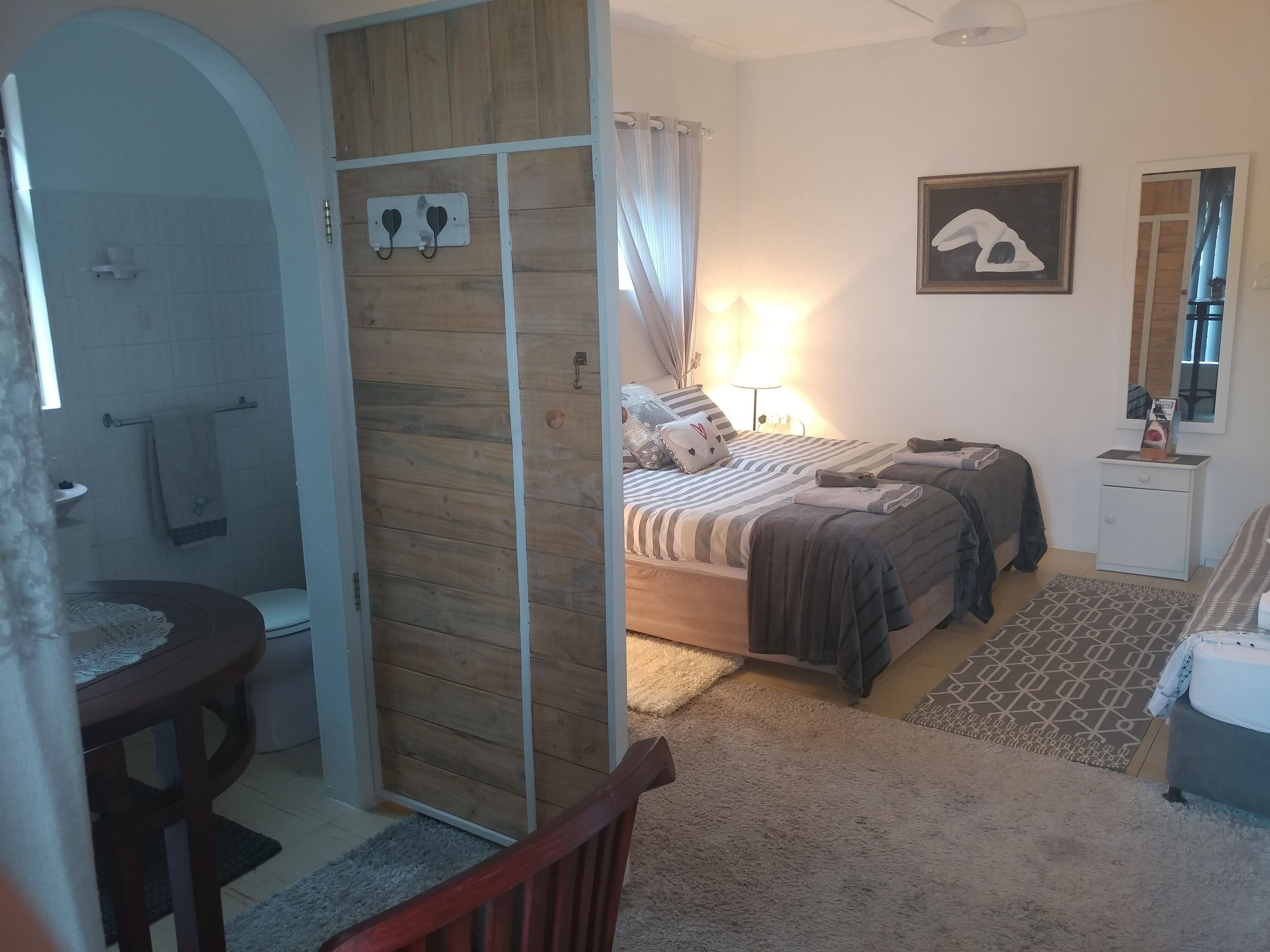 A bedroom with a bed, bedside tables, a nightstand, a mirror, and a shower area.