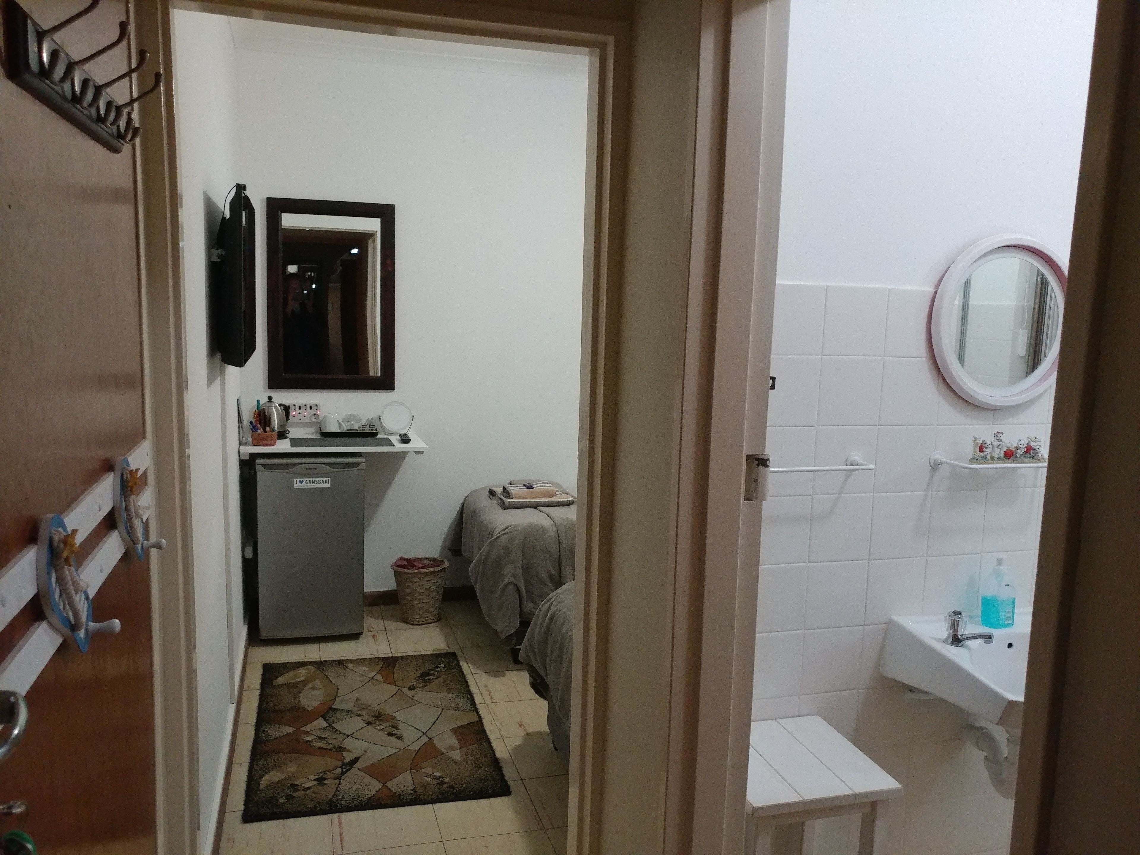 Une chambre d’hôtel compacte comprenant un coin cuisine, un lit, une petite salle de bain avec un lavabo et un miroir, et une porte donnant sur une autre pièce.