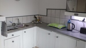 A kitchen with white cabinets, a stainless steel sink, a clock, a kettle, and a Samsung TV on a shelf. - After8 B&B (Kleinbaai)