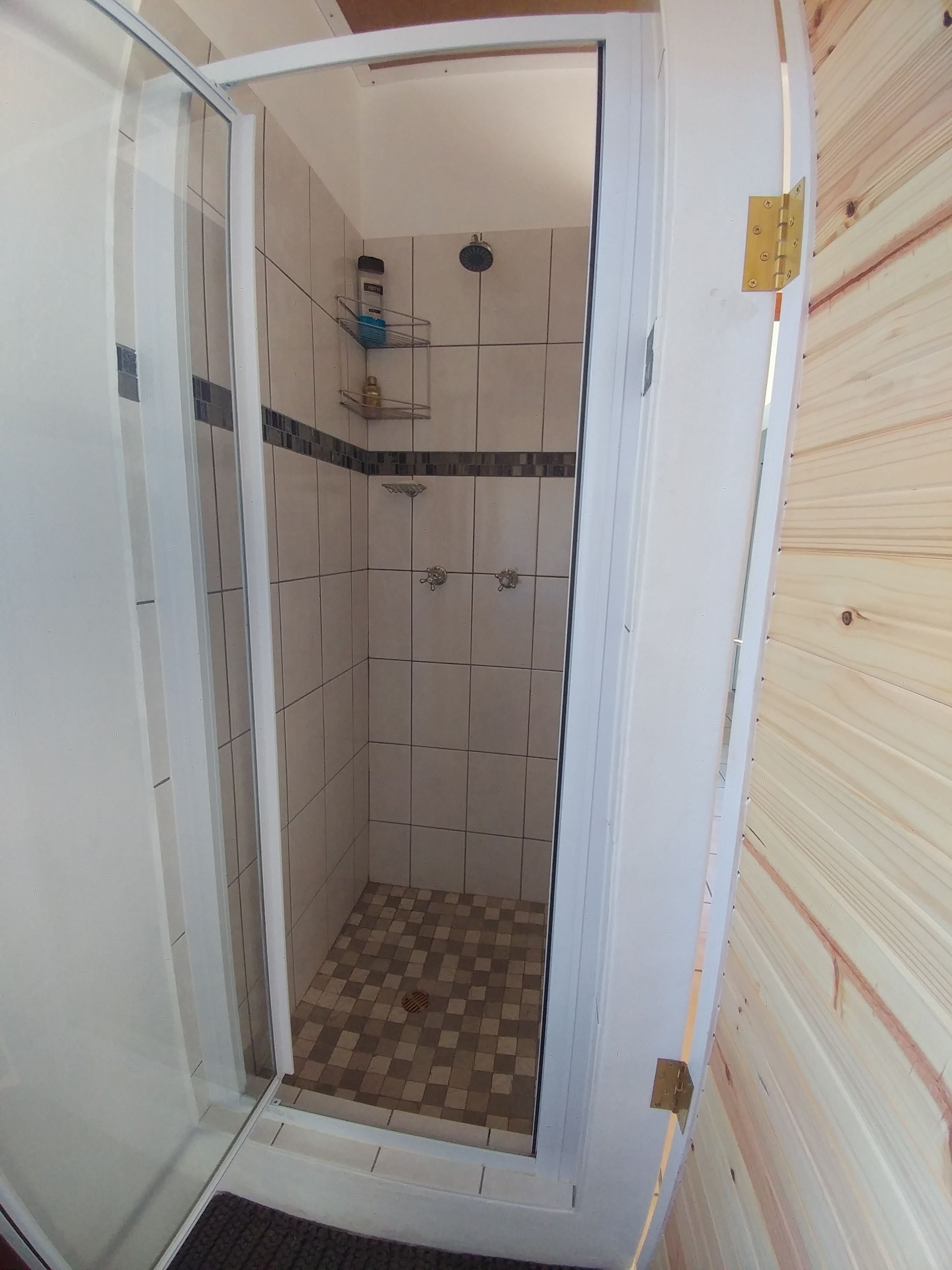 Eine Dusche mit gefliesten Wänden, einem Schachbrettmuster-Boden und einem Metallregal mit Toilettenartikeln.