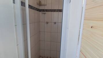 Eine Dusche mit gefliesten Wänden, einem Schachbrettmuster-Boden und einem Metallregal mit Toilettenartikeln.