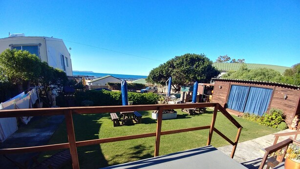 A patio area with a view of a grassy backyard, a wooden deck, and a building with a blue garage door. - After8 B&B (Kleinbaai)