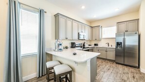 Une cuisine moderne dotée d’un îlot central, d’appareils électroménagers en acier inoxydable et d’un revêtement de sol en bois clair.