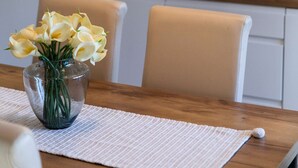 Una cuina amb armaris blancs, una aixeta d'acer inoxidable, una cuina de gas i un vas amb flors damunt la taula.