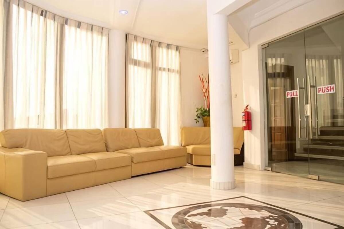 Un hall de hotel con un sofá beige, una puerta de vidrio con letreros que indican 'TIRAR' y 'EMPUJAR', un extintor y un suelo de baldosas.