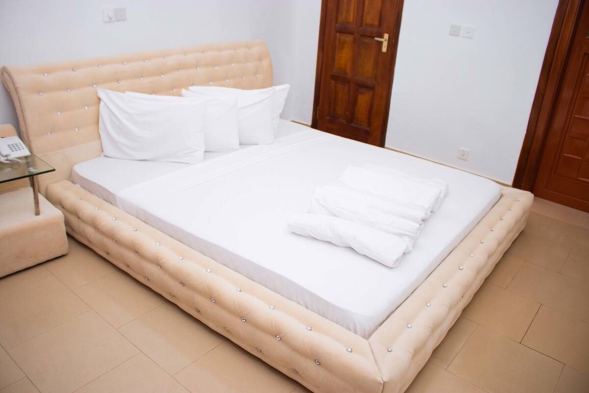 Un dormitorio con una cama grande, una mesita de noche de cristal y una puerta de madera.