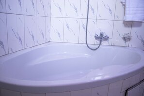 A bathroom with a white bathtub, a handheld showerhead, and a small shelf with a towel. - Odjidja Royal Palace Hotel (Taifa)