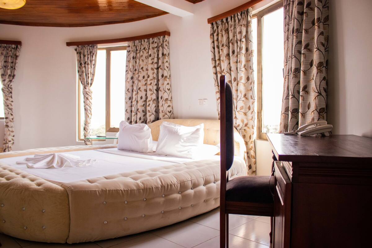Un dormitorio con una cama grande, un escritorio de madera y cortinas con estampado de hojas.