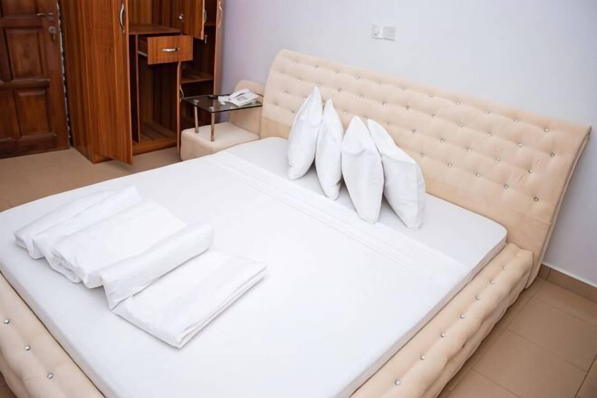 Una cama bien hecha con almohadas, una mesita de noche con lámpara y un armario de madera.