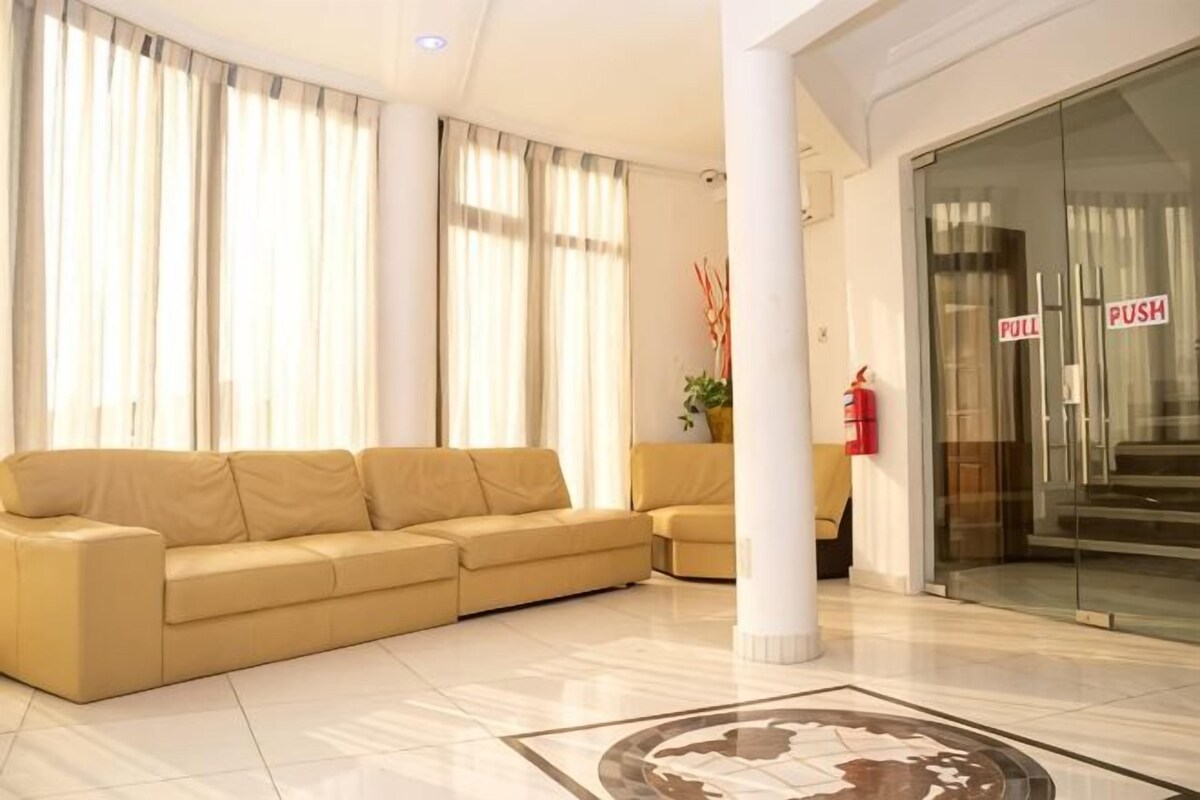 A hotel lobby with a beige sofa, a glass door with 'PULL' and 'PUSH' signs, a fire extinguisher, and a tiled floor.