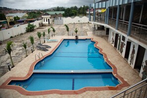 A rectangular swimming pool with a tiled edge, surrounded by a low wall and a few palm trees. - Odjidja Royal Palace Hotel (Taifa)