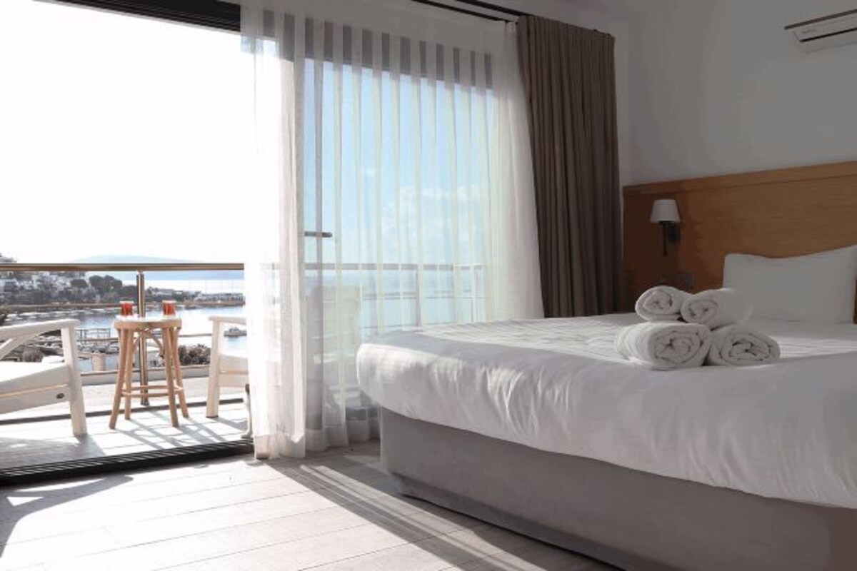 Ett hotellrum med en stor säng, utsikt över havet och en balkong med ett bord och stolar.