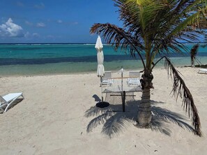 Una playa con una silla hamaca, una mesita y un paraguas blanco.
