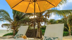 Eine Strandlounge mit weißen Liegestühlen und einem gelben Sonnenschirm.