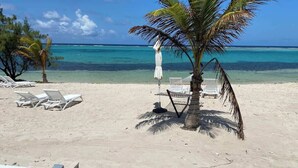 Ein Strand mit weißen Liegestühlen, einer Palme und einem Poolbereich.