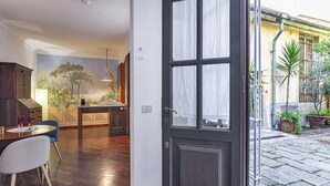 Eine offene Tür führt in einen Essbereich mit einem für zwei Personen gedecktem Tisch, einem blauen Stuhl und einem Holzschrank.