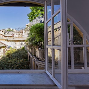 Une vue depuis une fenêtre donnant sur un bâtiment historique, avec un escalier et une végétation luxuriante.