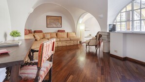 Ein geräumiges Wohnzimmer mit Holzboden, einem großen Sofa, einem Esstisch mit Stühlen und einem Fenster mit Blick.