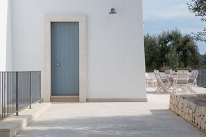 A white building with a blue door, outdoor seating area with white chairs, and a stone wall.