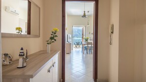 Un couloir doté d’un plancher en bois, d’un miroir, d’une petite table ornée d’un vase de fleurs, et d’où l’on aperçoit une salle à manger avec une table et des chaises.