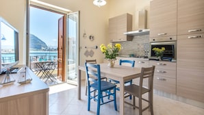 Une cuisine moderne avec des meubles en bois, un coin repas avec des chaises bleues et une vue sur la mer par une porte vitrée.