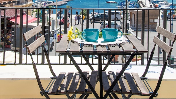 Un balcon avec une table et des chaises donnant sur une zone côtière, avec des bateaux et une montagne en arrière-plan.
