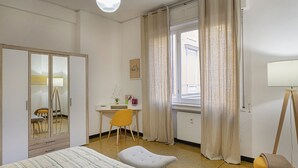 Habitación de hotel con cama, escritorio, silla, espejo y ventana con cortinas.