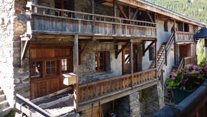 Un edificio rústico de madera con fachada de piedra, que cuenta con un balcón con barandillas de madera y una escalera que conduce a un nivel superior.