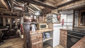 Una cocina rústica con vigas de madera, pared de piedra, microondas y estufa.