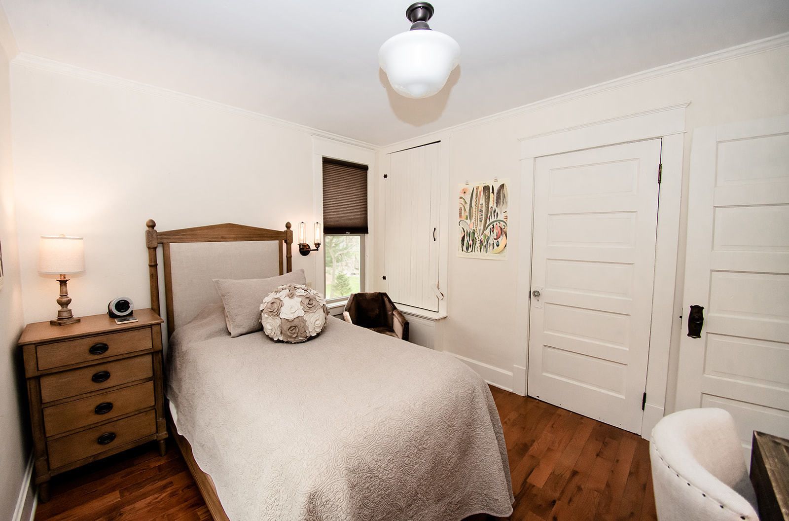 Een slaapkamer met een houten hemelbed, een nachtkastje met een lamp, een stoel en een deur met een decoratief paneel.