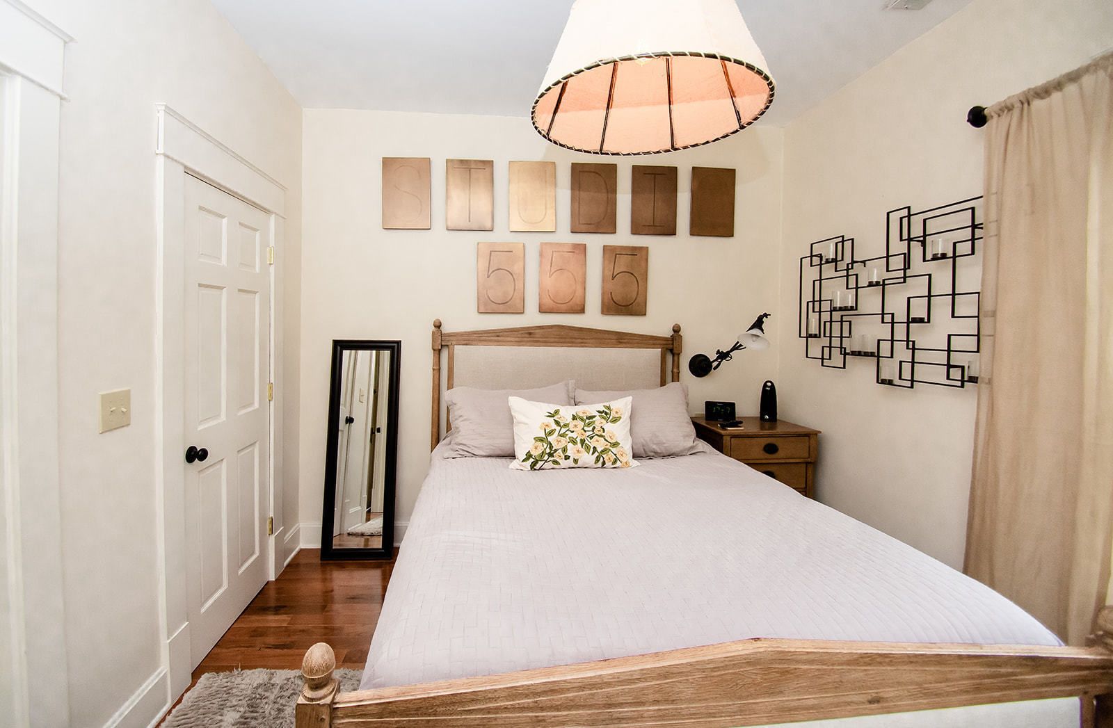 A bedroom with a wooden bed, a bedside table with a lamp, a mirror, and wall art.