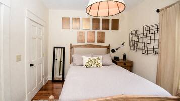 A bedroom with a wooden bed, a bedside table with a lamp, a mirror, and wall art.