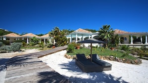 Een resort met een houten terras, ligbedden en een overdekt gedeelte met een palmboom.