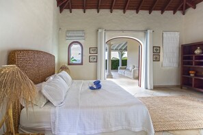 A bedroom with a bed, a wicker headboard, a woven rug, and a view of an outdoor patio.