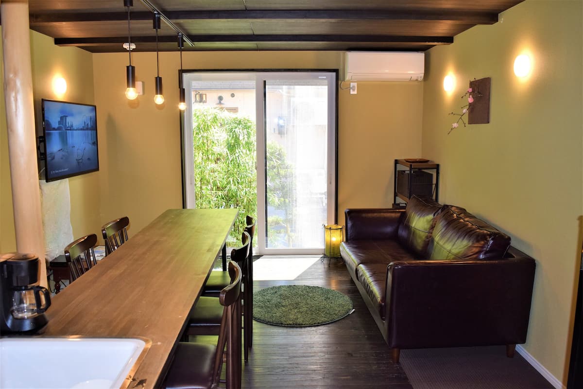 A dining area with a wooden table and chairs, a sofa, and a television on the wall.